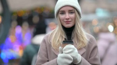 Şenlik şehir fuarında arka planda bir fincan sıcak kahveyle yürüyen gülümseyen genç bir kızın portresi. Olumlu ruh hali mutlu duygu dışarıda duruyor..