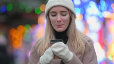 Şirin genç bir kız, festivaldeki Noel ışıklarının arka planında sıcak kahve içiyor. Olumlu ruh hali mutlu duygu dışarıda duruyor. Mutlu yıllar.