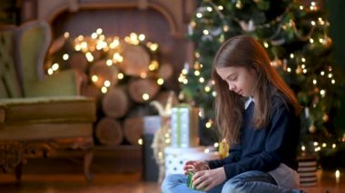 Noel ağacının yanında yerde oturan sevimli küçük bir kız hediyeleri açıyor. Noel hediyesini açan mutlu kız kutuya bakıyor. Tatil ve kutlama konsepti