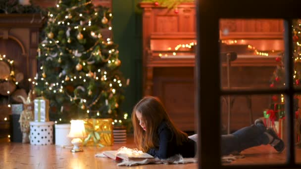 Ευτυχισμένο Κοριτσάκι Βρίσκεται Στο Πάτωμα Στο Φόντο Ενός Εορταστικού Χριστουγεννιάτικου — Αρχείο Βίντεο