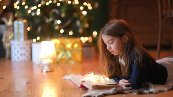 Słodka Dziewczynka Leży Podłodze Tle Świątecznej Choinki Czyta Książkę Tło — Wideo stockowe