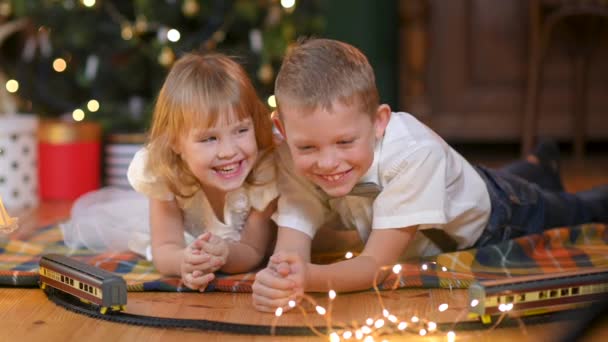 Szczęśliwe Dzieci Leżą Podłodze Tle Świątecznej Choinki Bawiąc Się Bawiąc — Wideo stockowe