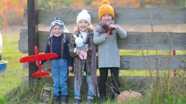 Mutlu aile çocukları kırsaldaki bir sonbahar tarlasında birlikte. Oyuncaklı bir grup neşeli çocuk ahşap bakım arka planında dostça duruyor. Mutlu gülen çocuklar.