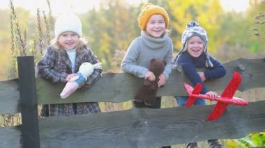 Mutlu aile çocukları kırsaldaki bir sonbahar tarlasında birlikte. Ahşap çitin üzerinde oyuncakları olan bir grup neşeli çocuk. Mutlu gülen çocuklar.
