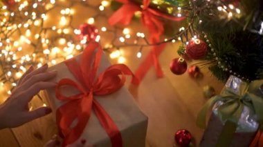 Kadınların elleri Noel ağacının altından büyük bir hediye kutusu alır ve kırmızı kurdeleyi çözer. Tatil ve Hediye Konsepti.