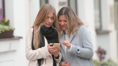 Dışarıda cep telefonu kullanan mutlu iki bayan arkadaşın portresi. Dışarıda cep telefonunu tutan gülümseyen kız. İletişim, sosyal ağlar, alışveriş kavramı.