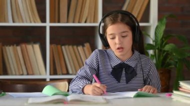 Masada oturmuş ödev yapan, deftere yazı yazan ve müzik dinleyen küçük bir kızın portresi. İlköğretim, okul kavramı.