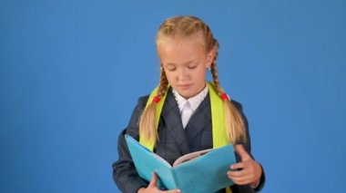 Sırt çantalı okul üniformalı mutlu kız öğrenci sarı bir stüdyo geçmişi olan bir kitap okuyor. okul konseptine geri dön