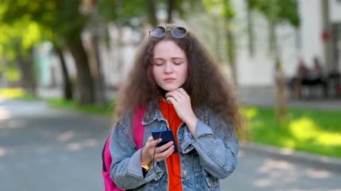 Şehir Sokağında Akıllı Telefonla İletişim kuran Koruyucu Maskeli Genç Çekici Kız. Maskeyi çıkarıyor ve üzülüyor. Genç nesil Z, şehirdeki telefon ile etkileşim halinde.