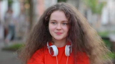 Kulaklıklı güzel Avrupalı kız şehirde sokakta kameraya bakıyor. Halk tarzı kavram.