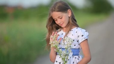 Bir yaz parkında elbise giymiş mutlu küçük bir kızın yakın plan portresi. Şirin Çocuk gülümsüyor ve dışarıda eğleniyor. Pozitif Çocuk. Mutlu çocukluk kavramı.
