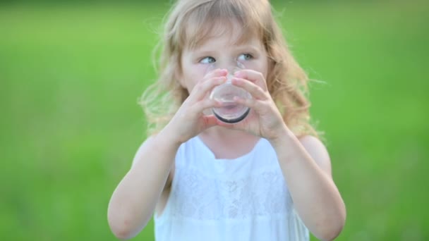 Piccola Ragazza Bionda Abito Bianco Beve Acqua Bicchiere All Aperto — Video Stock