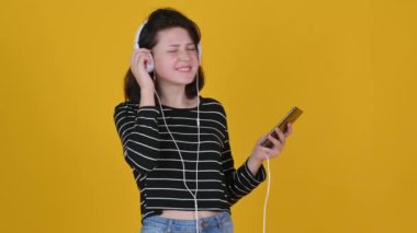 Kulaklıklı genç kız sarı arka planda müzik ve danslar dinliyor. Smartphone 'da yeni Müzik Uygulaması Kullanılıyor