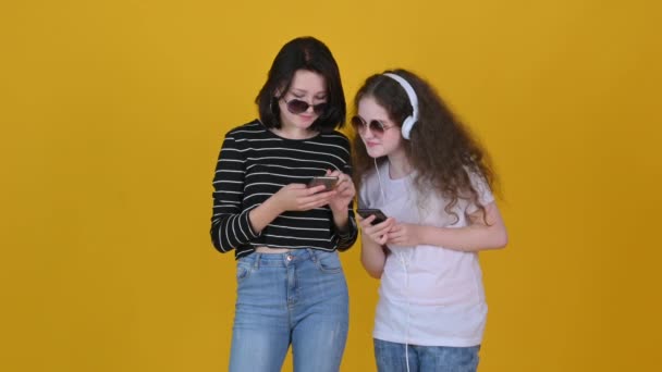 Jovens Amigas Usam Smartphones Ouvindo Música Isolada Fundo Amarelo — Vídeo de Stock