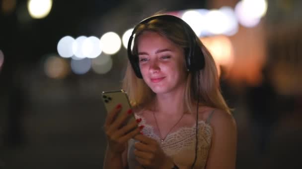 Nuori Onnellinen Nainen Kuuntelee Musiikkia Kuulokkeiden Kautta Street Night Townissa — kuvapankkivideo