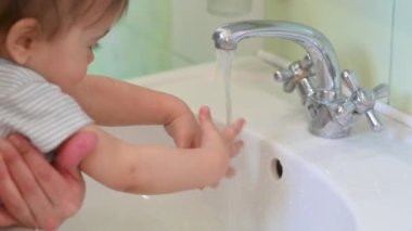 Banyodaki bebek ellerini yıkıyor ve su ellerinden akıyor. Koronavirüsü önleme. Yıkama. Temiz el kavramı