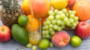 Taze meyve suyu, bahçedeki ahşap bir masanın üzerindeki bir bardağa dökülüyor, bir sürü meyvenin etrafına. Sağlıklı gıda konsepti. Meyve karışımı..