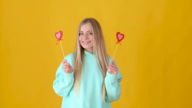 Sarışın bir kızın portresi. Elinde kırmızı bir kalp tutuyordu ve sarı bir arka planda izole bir şekilde gülümsüyordu. Sevgililer Günü konsepti. Anneler Günü. Kadınlar Günü