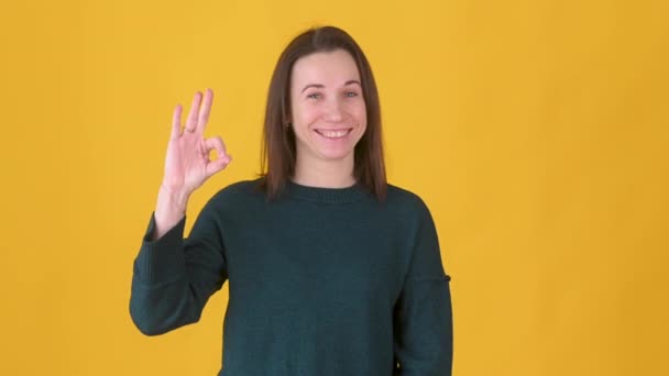 肖像画の若い女の子のカメラの魅力的な笑顔を見て をジェスチャー黄色の背景に隔離されたOkを示す 人々のライフスタイルコンセプト — ストック動画