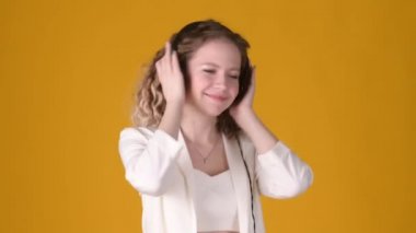 Kıvırcık saçlı, kulaklıklı neşeli genç kız sarı arka planda müzik dinliyor ve dans ediyor. Smartphone 'da yeni Müzik Uygulaması Kullanılıyor