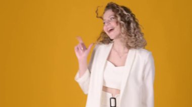 Sarı arka planda izole edilmiş fotokopi alanı çalışma alanında kıvırcık saçlı ve parmaklarını kenarda gösteren neşeli genç kız. Halk yaşam tarzı konsepti.