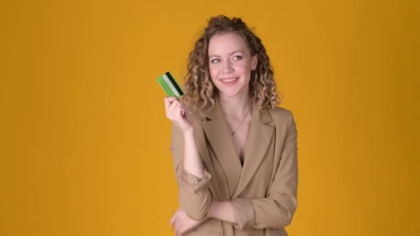 黄色のスタジオバックで隔離されたジェスチャーのように親指を示すクレジットカードに巻き毛ポイント手で陽気な若い女の子 人々のライフスタイルコンセプト — ストック動画