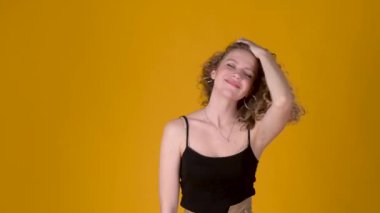 Yavaş hareket eden mutlu, kaygısız, kıvırcık saçlı dans eden ve sarı arka plandaki kameraya bakan genç kız. Halk yaşam tarzı konsepti