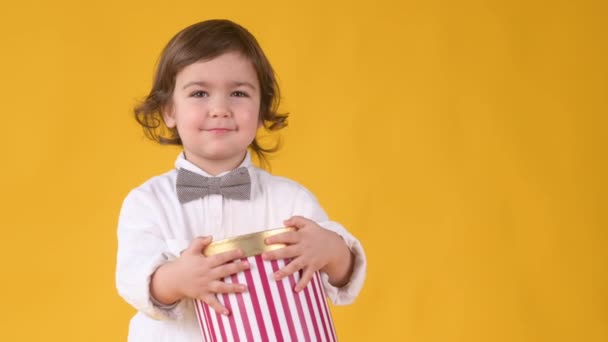 小さな面白い男の子は大きなギフトボックスを手に持っていて 黄色のスタジオの背景で陽気に笑います 誕生日プレゼントサプライズ ホリデーお祝いコンセプト — ストック動画