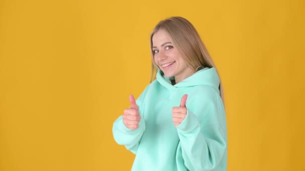 正面的年轻女孩在黄色的工作室背景下摆出孤立的姿势 女人赞许地看着镜头 竖起大拇指 好像是积极的信号 人的生活方式概念 — 图库视频影像