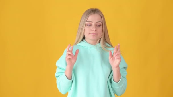 巻き毛の若い魅力的な女の子は 彼女の指で願いを黄色のスタジオの背景に交差させます 人々のライフスタイルコンセプト — ストック動画