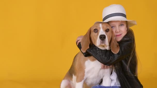 Linda Niña Sombrero Abraza Perro Beagle Sobre Fondo Amarillo Estudio — Vídeo de stock