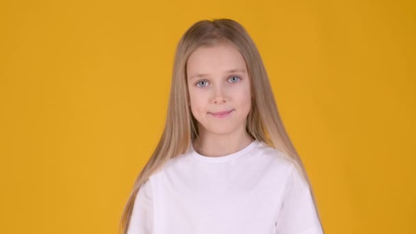 白いTシャツの面白い小さなブロンドの女の子は笑顔と黄色のスタジオの背景にポーズ 子供時代のライフスタイルのコンセプト — ストック動画