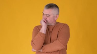 Sarı stüdyo geçmişine karşı zor bir seçim üzerine düşünen yaşlı, gri saçlı bir adam portresi. İnsanlar fikirlerini düşündükçe şaşırıyor