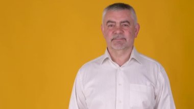 Neşeli yaşlı gri saçlı adam sarı arka planda izole edilmiş fotokopi alanı çalışma alanını işaret ediyor. Halk yaşam tarzı konsepti.