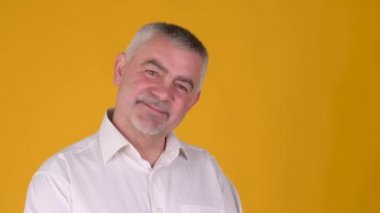 Neşeli yaşlı, gri saçlı bir adamın portresi gülümseyen ve sarı bir stüdyo arka planında kameraya bakan. Halk yaşam tarzı konsepti.