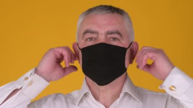 Sarı arka planda izole edilmiş, koruyucu maskeli, kendinden emin, beyaz, üst düzey bir adamın portresi..