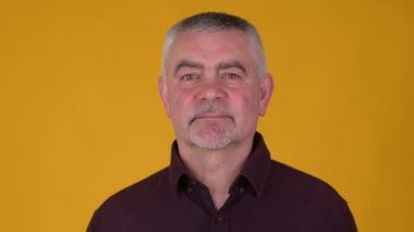 Neşeli yaşlı, gri saçlı bir adamın portresi gülümseyen ve sarı bir stüdyo arka planında kameraya bakan. Halk yaşam tarzı konsepti.