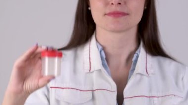 Tıbbi üniformalı bir kadın doktorun portresi beyaz arka planda izole edilmiş bir test konteynırını tutuyor. Tıbbi testler için plastik kavanozlar.