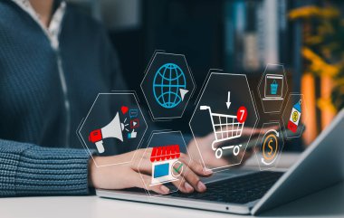 Çevrimiçi alışveriş ve e-ticaret teknolojisi internet kavramı. Diz üstü bilgisayar ve akıllı telefon kullanan kadın ekommersi, sosyal medya, İnternet perakendecisi, çevrimiçi alışveriş ve dijital pazarlamayı temsil eden ikonlar kullanıyor.