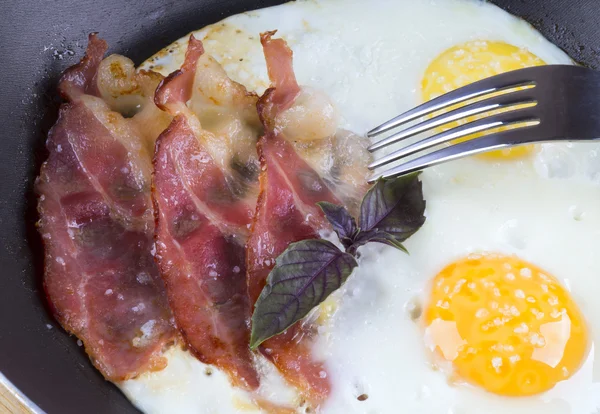 Жареные яйца и бекон в сковороде едят вилкой — стоковое фото