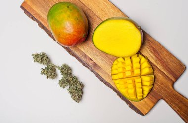 Kenevir tomurcuklarıyla mango meyvesi kes. Mangolardaki Myrcene ve terpenes THC 'nin esrar üzerindeki etkilerini destekler. Beyaz zemin üzerinde ahşap kesim plakası.