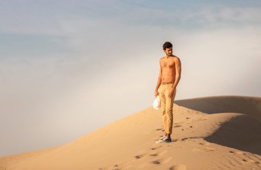 Genç Arap üstsüz adam çölde poz veriyor.