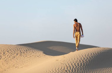 Genç Arap üstsüz adam çölde tek başına yürüyor.