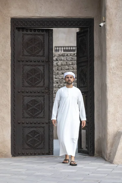 Dubai 'nin tarihi Shindagha bölgesinde geleneksel giysiler içinde Arap bir adam kapıdan çıkıyor.