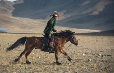 Bayan Ulgii, Ekim 2015: Kazak kartal avcısı, geleneksel kıyafetler içinde, ata biniyor.