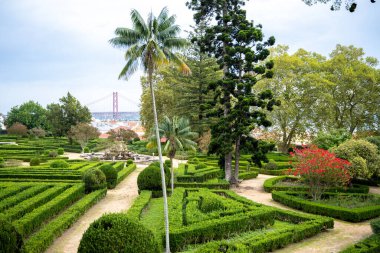 Lizbon 'daki Ajuda Botanik Bahçesi' nin geniş manzarası. Geometrik çitler, merkezi bir çeşme ve Tagus Nehri üzerindeki 25 de Abril Köprüsü..