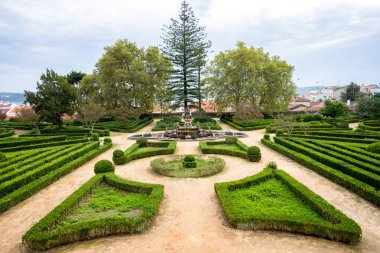 Geometrik çitler, Belem Lizbon 'da arka planda çatıları olan merkezi bir çeşmeye giden simetrik bahçe yolları oluşturur. Fotoğraf: 4 Kasım 2025.