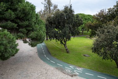 Olgun ağaçlar ve Lizbon Portekiz 'de kaldırım taşları olan yeşil bir parktaki bisiklet yolu. Bulutlu bir günde huzurlu bir açık hava dinlenme alanı.
