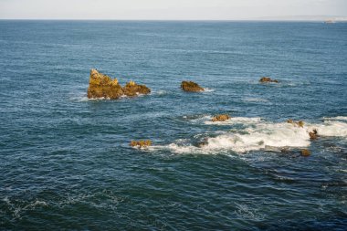 Sivri kıyı kayaları Peniche Portekiz 'den gelen küçük dalgalarla okyanusun yüzeyini kırıyor..