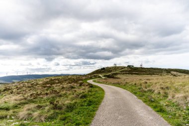 Serra de Montejunto Portekiz 29 Kasım 2025. Dar asfaltlı yol uzak yel değirmenlerine doğru açık yamaçtan geçiyor..